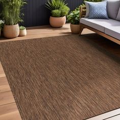 a brown area rug on top of a wooden floor next to a couch and potted plants