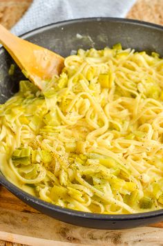 a pan filled with noodles and broccoli on top of a wooden cutting board