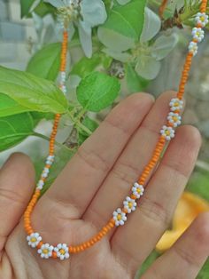 a hand holding an orange and white beaded necklace on it's left wrist