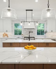 a bowl of oranges sitting on top of a kitchen counter next to two lights