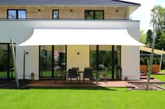 a large white awning in front of a house with patio furniture on the grass