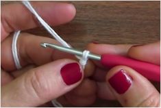 two hands with red nail polish are holding a crochet hook