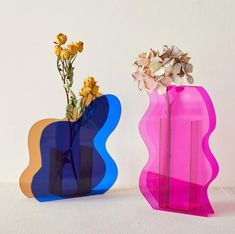 two colorful vases with flowers in them on a white tableclothed surface next to each other