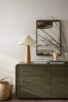 a green dresser with a lamp on top and a painting above it in the corner