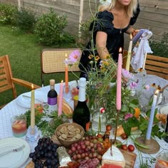 a woman standing in front of a table filled with food and drinks, surrounded by candles