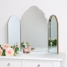 a white dresser topped with two mirrors and flowers