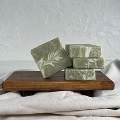 three bars of soap sitting on top of a wooden board next to a white cloth