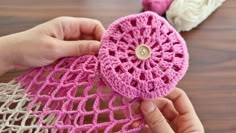 someone is crocheting a piece of pink yarn with a wooden button on it