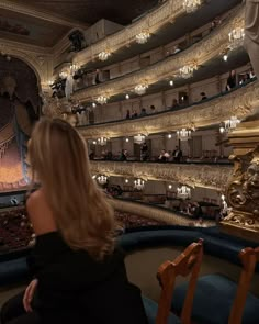 a woman is sitting in front of an auditorium full of people and looking at the stage