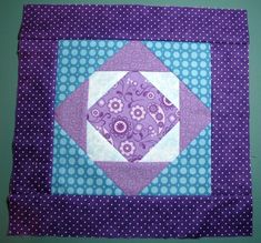 a purple and blue quilted square with white dots on the bottom, in front of a green wall