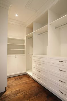 an empty walk in closet with white cabinets and drawers on the wall, along with wood flooring