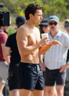 a shirtless man holding a coffee cup in front of a group of people on the beach