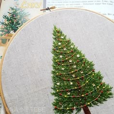 a cross stitch christmas tree is on the table next to an open book and scissors