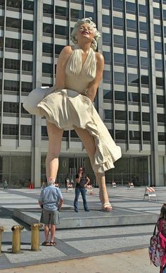 a statue of a woman in front of a building with people standing around and looking at it