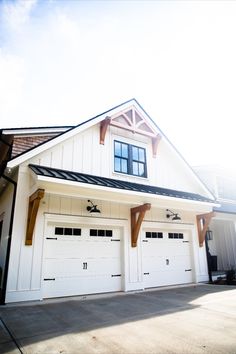 farmhouse Bomber LED gooseneck lights above dual garage doors, Barn Light Electric Outdoor Light Above Garage, Awning Above Garage Door, Farmhouse Exterior Lighting Garage, Decorative Garage Overhang, White Garage With Wood Doors, White And Black House Exterior With Wood, Pergola Over Garage Door Wood, Garage Awnings Exterior, Exterior Lights Above Garage Doors