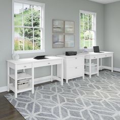 a computer desk sitting in the middle of a room next to two windows and a rug on the floor