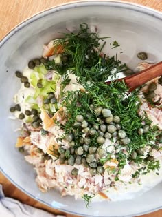 a white bowl filled with lots of food on top of a wooden table next to utensils