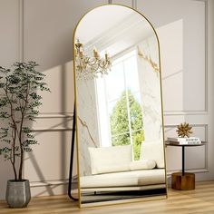 a mirror sitting on top of a wooden floor next to a white couch and potted plant