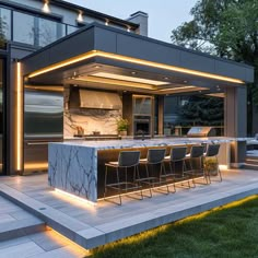 an outdoor kitchen is lit up at night with lights on the counter and bar stools