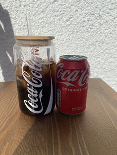 a soda can sitting on top of a wooden table next to a glass with coca - cola in it