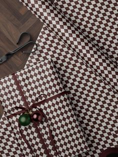 a pair of scissors sitting on top of brown and white checkered fabric next to a green ornament