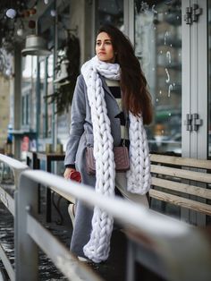 a woman standing on a bench in front of a building wearing a scarf and coat