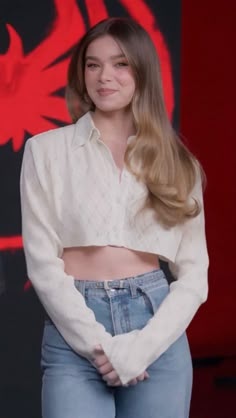 a woman with long blonde hair standing in front of a red and black background wearing jeans