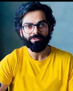 a man with glasses and a beard wearing a yellow t - shirt is looking at the camera