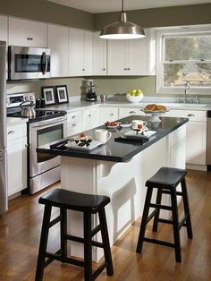 a kitchen with white cabinets, black counter tops and two stools in front of the island