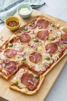 a pizza with pepperoni, onions and green olives on a cutting board next to other ingredients