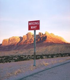 a red wrong way sign sitting on the side of a road next to a mountain