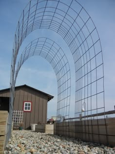 an arch made out of metal wire sitting on top of a gravel covered ground next to a building