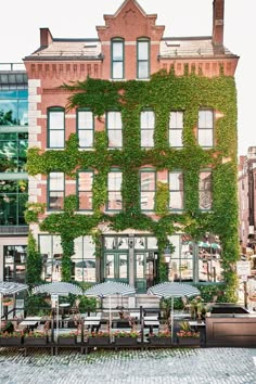 an ivy covered building with tables and umbrellas on the sidewalk in front of it