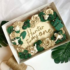 a cake in a box that says hunter thinsone on the side with green leaves around it