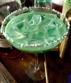 a close up of a green drink in a glass on a table next to bottles