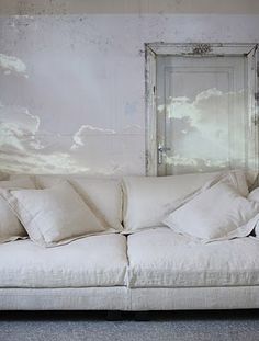 a white couch sitting in front of a wall with clouds painted on it's walls