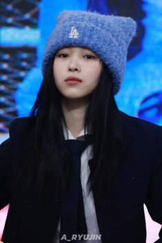 a girl with long black hair wearing a blue hat and tie in front of a screen