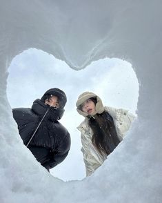 two people standing in the snow looking at each other through a heart - shaped hole