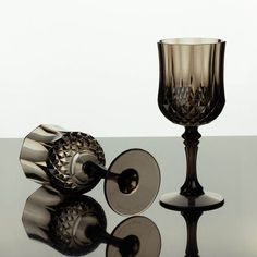 two glass goblets sitting next to each other on top of a reflective surface