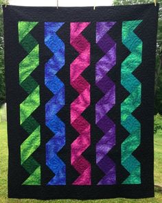 a colorful quilt hanging from a clothes line in the grass with trees in the background