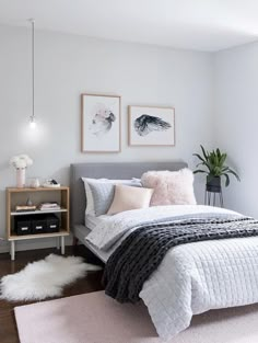 a bedroom with white walls and gray bedding, two framed pictures on the wall