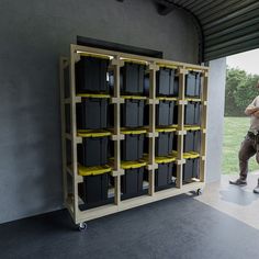 a man standing in front of a storage unit with bins on the back and yellow shelves