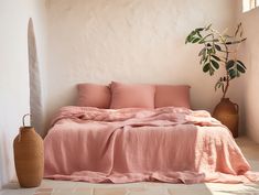 a bed with pink sheets and pillows next to a potted plant on the floor