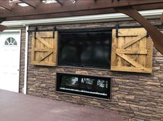 a tv mounted to the side of a brick wall with wooden shutters on it