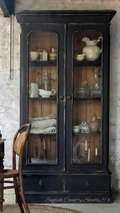 an old china cabinet with glass doors and shelves in the corner, next to a chair