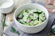 a white bowl filled with cucumbers on top of a table next to garlic