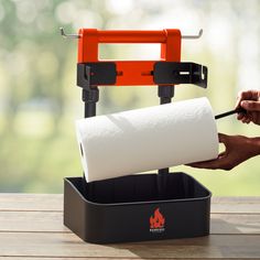 a person is holding a roll of toilet paper in front of an orange and black holder