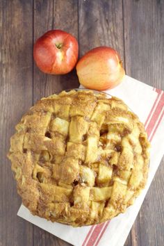 an apple pie sitting on top of a wooden table next to two pieces of fruit