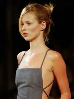 a woman is walking down the runway with her hand on her hip while wearing a gray dress