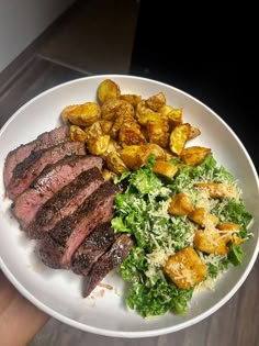 a white plate topped with steak, potatoes and lettuce on top of a wooden table